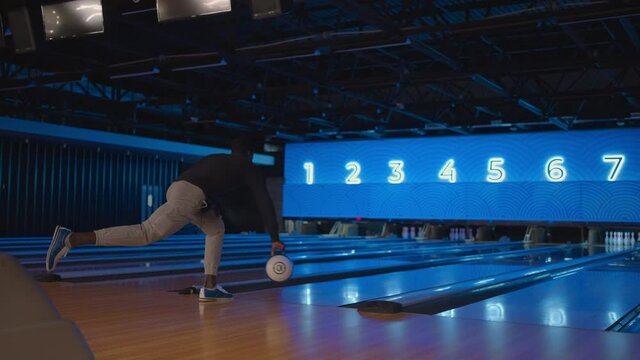 A black man bowling man throws a ball in slow motion and knocks down skittles. Play bowling. Throw balls on the floor of the bowling club