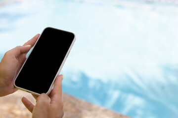 Female hand holding smartphone near swimming pool. Closeup, mock up.