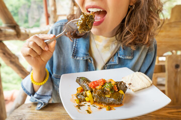Happy woman eats delicious dolma, a traditional Armenian and Georgian dish made of minced meat wrapped in grape leaves