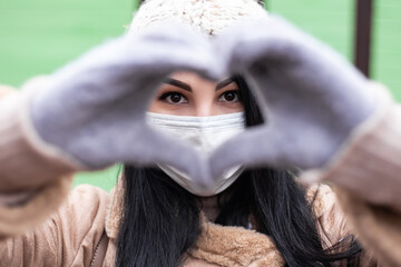 Pretty woman gesturing celebrating dressed warm coat show making hands heart sign love shape. Cold weather, winter market holidays fair, travel resort. New Year Christmas decorations
