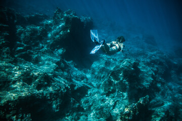 Naklejka na ściany i meble Underwater shooting girl dives underwater freediving in a black swimsuit in clear water