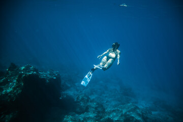 Underwater shooting girl dives underwater freediving in a black swimsuit in clear water