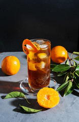 Chinotto drink in the glass with ice and fruits on the grey table