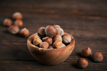 Pile of hazelnuts filbert in a wooden bowl on a dark wooden background