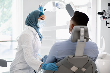 Fototapeta premium Stomatologic Check Up. Muslim Female Dentist Doctor Having Appointment With Male Patient