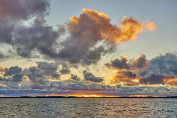 A colorful sunset on the Baltic Sea with clouds illuminated by the sun setting over the horizon.