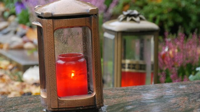 Red memorial candle burning with fire on rainy day on tombstone in cemetery autumn, rainy day. Grave with tombstone on which raindrops falling, against abackground of yellow foliage. Day of all dead