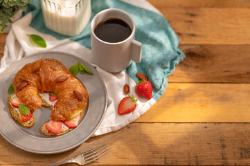 Fragrant croissant with butter, strawberries, mint and almonds .. A cup of coffee and a jug of milk. Wood texture, turquoise white napkin. High angle view. Home comfort, recipe book, culinary blog.