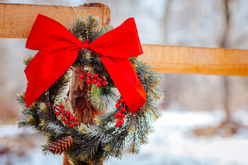 Christmas wreath with red bow are on a wooden fence against winter forest