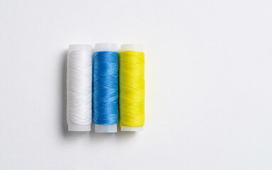 Three spools of thread for sewing are stacked in the form of the flag of Canary Islands on a white background. There is a free empty space.