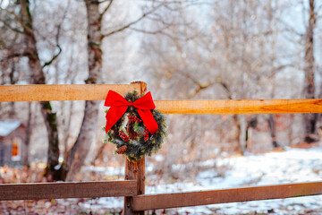 Christmas wreath with red bow are on a wooden fence against winter forest