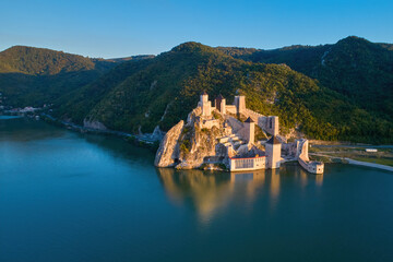 The medieval fortress of Golubac against iron gate of national park Djerdap, mirroring in the waters of the Danube. Colorful sunset light, blue sky. Aerial shot. Famous tourist place, Serbia.