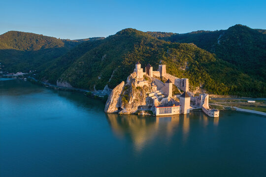 The medieval fortress of Golubac against iron gate of national park Djerdap, mirroring in the waters of the Danube. Colorful sunset light, blue sky. Aerial shot. Famous tourist place, Serbia.