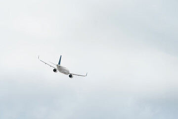 Rear view of a white passenger plane in close-up against a gray sky with copy space. Plane is heading to the right - Powered by Adobe