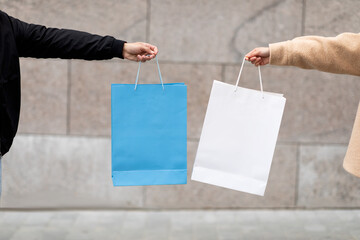 Cropped view of young man and woman holding shopping bags with mockup for your brand logo near stone wall