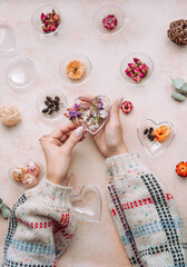 Woman filling heart shape ornament with dried flowers on beige concrete background