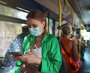 Woman in medical mask with mobile phone in the bus.