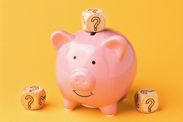 Wooden cubes with a question mark near a piggy bank on a colored background, the concept of...