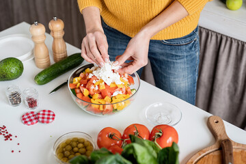 Front view of female hands making salad cutting feta cheese in the kitchen