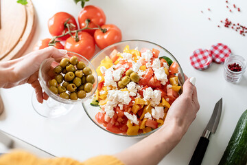 female hands making greek salad adding olives to the bowl