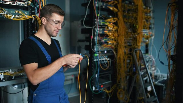 Young man in uniform testing internet equipment by using special device in server room