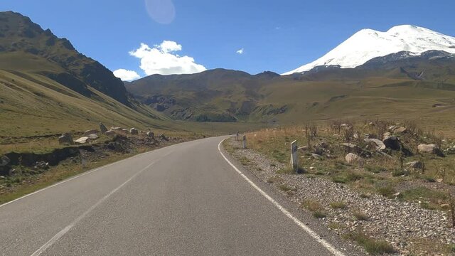 Fragment of the road to Mount Elbrus, North Caucasus. Filming from a car moving on road, first-person video. Elbrus, hills, horses, campers and rubbish along the road.