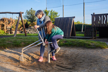 mother with her daughter playing on a big toy excavator in a playground