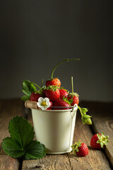 juicy red strawberries in a mini bucket on a wooden background. High quality photo