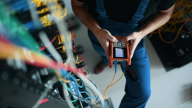 Young man in uniform testing internet equipment by using special device in server room