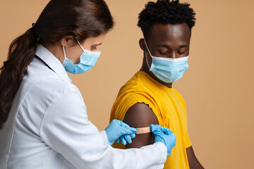 Female Nurse Applying Plaster On Black Guy's Shoulder After Injection Shot