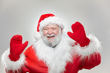 Happy Santa Claus dressed in a red coat, with gloves and a hat, with his hands raised high isolated gray background.