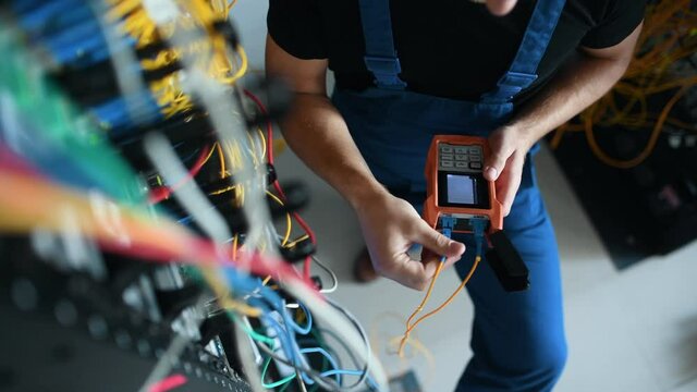 Young man in uniform testing internet equipment by using special device in server room