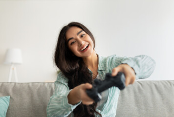 Joyful Indian woman with joystick playing online video games, having fun in living room © Prostock-studio