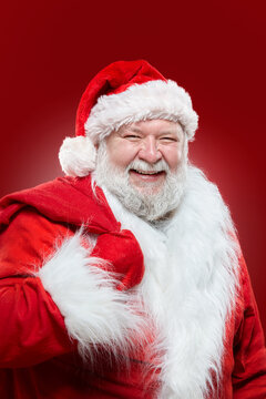 Closeup image of a happy laughing Santa Claus dressed in a red coat and a hat, keep a bag on his back, isolated red background.