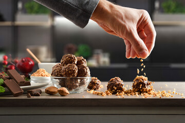 Preparing chocolate balls with almond chips on a kitchen bench