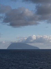 Corvo Island shrouded in fog and clouds, seen from Flores Island, in the foreground the Atlantic Ocean.