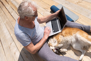 An elderly man is playing with a dog sitting on the terrace and working at the computer after yoga...