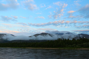 Heavenly landscape in the morning at dawn with white clouds illuminated by the sun in the blue sky with fog in the mountains spreading over the forest and the lake