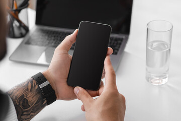 Middle aged caucasian male at workplace with laptop, checking mail, app and social networks on smartphone