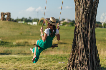 beautiful girl in a hat swinging on a swing in the park