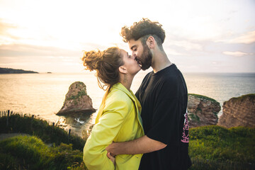Young heterosexual couple embracing each other at the top of a cliff near the ocean.