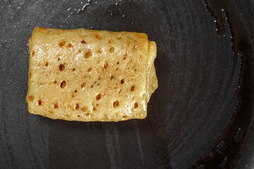 The stuffed pancake lies on a Teflon frying pan, greased with oil.