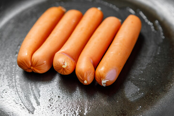 Beef sausages lie in a frying pan with a non-stick coating, greased with oil. Cooking at home.
