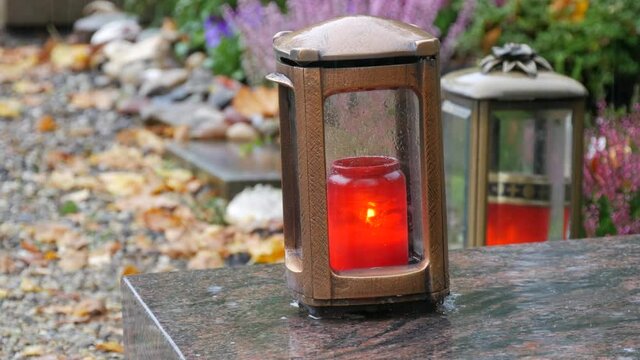 Red memorial candle burning with fire on rainy day on tombstone in cemetery autumn, rainy day. Grave with tombstone on which raindrops falling, against abackground of yellow foliage. Day of all dead