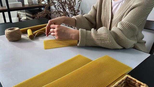 Woman cuts sheet of beeswax with honeycomb texture to make decorative candle at table in workshop closeup timelapse