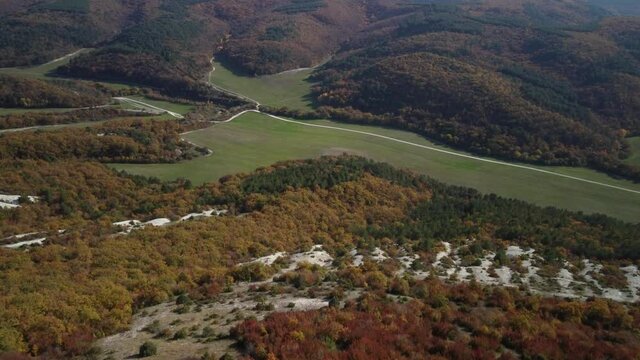 Flying over the valley in the Mangup gorge. Colorful trees and a green meadow. Bright colors of the Crimean autumn. 4k drone video