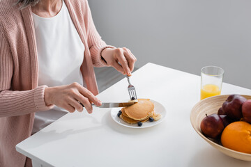 Fototapeta na wymiar Cropped view of woman cutting pancakes near fresh fruits and orange juice in kitchen.