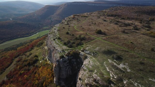 Flying over the cliff in the Mangup gorge. The edge of the white cliff rises above the bright trees. Bright colors of the Crimean autumn. 4k drone video