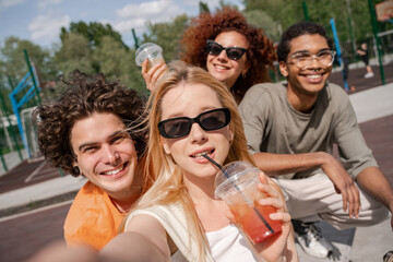 young woman in sunglasses drinking refreshing cocktail near happy multiethnic friends.