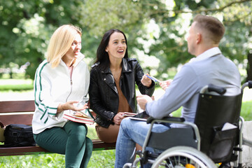 Plakat Two young women communicate with a man in wheelchair in park